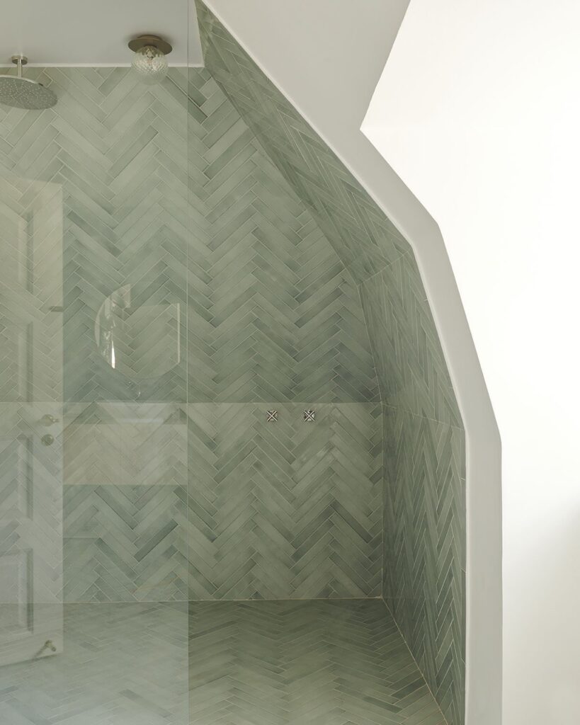 A jade-toned herringbone bathroom wall and floor underneath a sloped ceiling