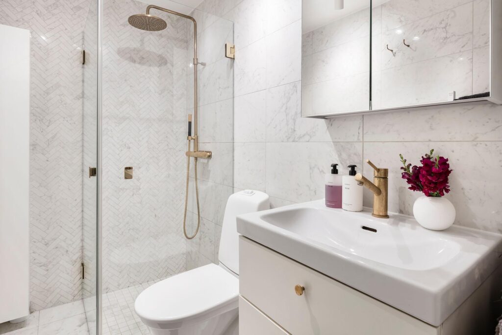 A herringbone tile shower wall paired with marble tiling on the bathroom wall