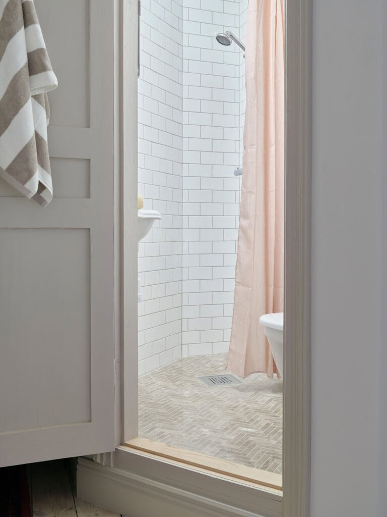 An asymmetrical bathroom with subtle beige herringbone floor tiles and white tiles on the wall