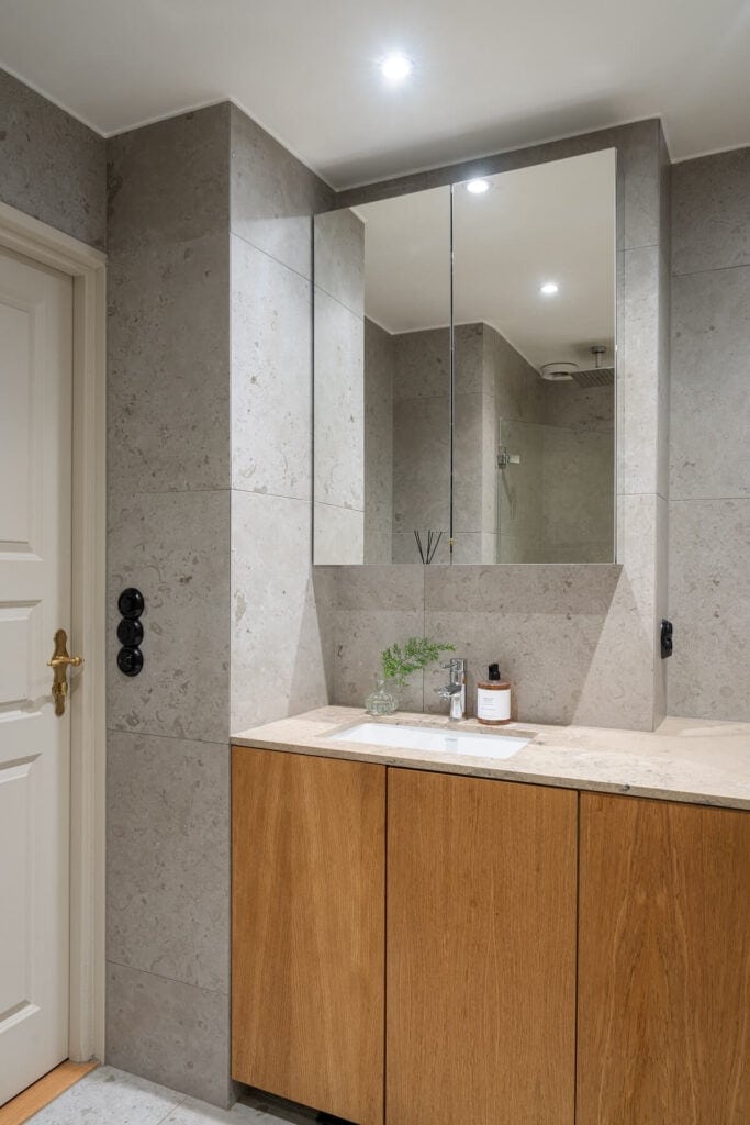 A modern bathroom with large limestone tiles, paired with an oak vanity