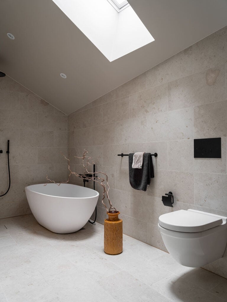 A limestone attic bathroom paired with a minimal white soaking tub and black fixtures