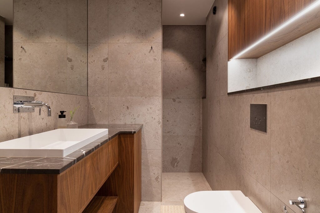 Beige limestone tiles on the walls and floors, paired with a black marble counter and natural wood tones