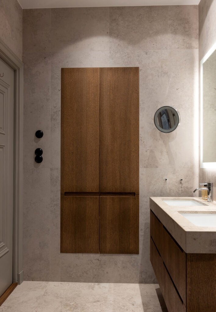 A beige limestone bathroom with a dark oak vanity and cupboard doors