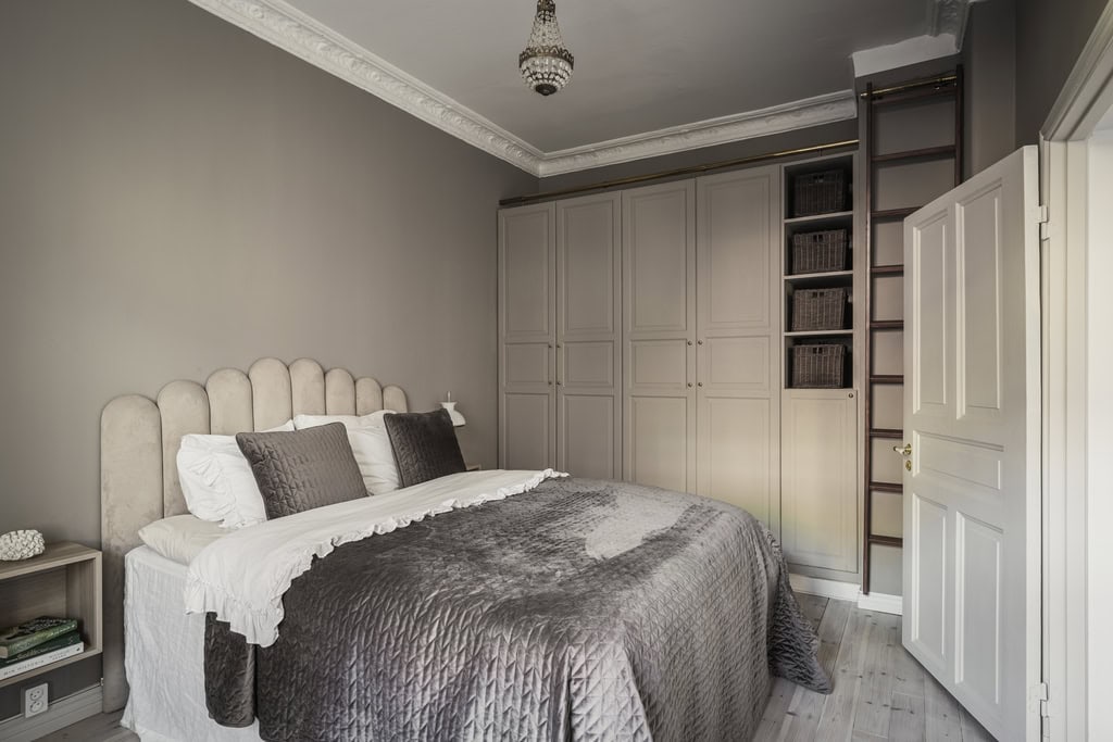 A beige wardrobe with woven baskets and a ladder to reach the upper shelves