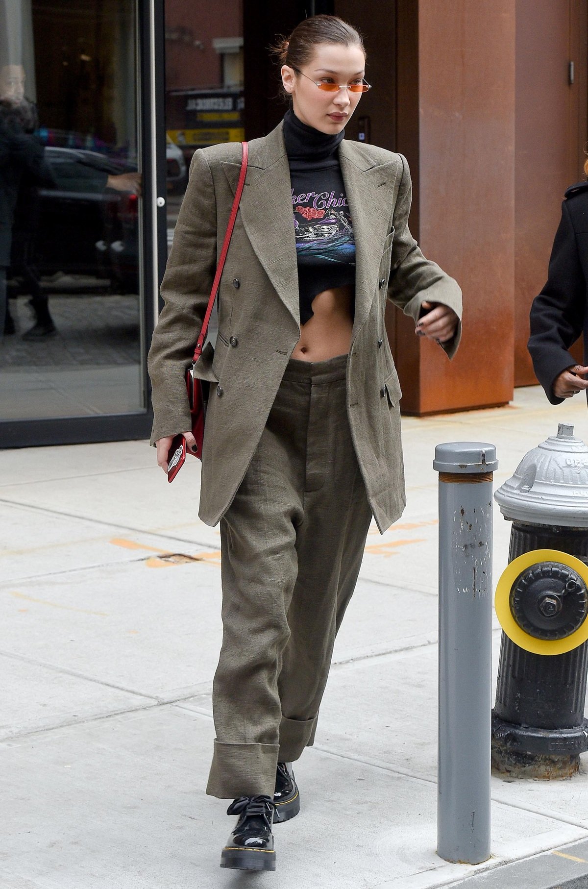 Bella Hadid elevates her street style in New York City on February 9, 2018, pairing oversized Vivienne Westwood tailoring with edgy Dr. Martens Holly Lolita platform oxfords, Christianahjones orange sunglasses, and a playful Prada comic-print bag