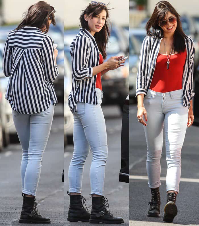 Daisy Lowe effortlessly styles a bold yet casual look near her London home, pairing a black-and-white striped shirt with an orange vest and light-wash skinny jeans, finishing the outfit with classic Dr. Martens boots and oversized aviator sunglasses—a perfect blend of edgy and chic for a summer day