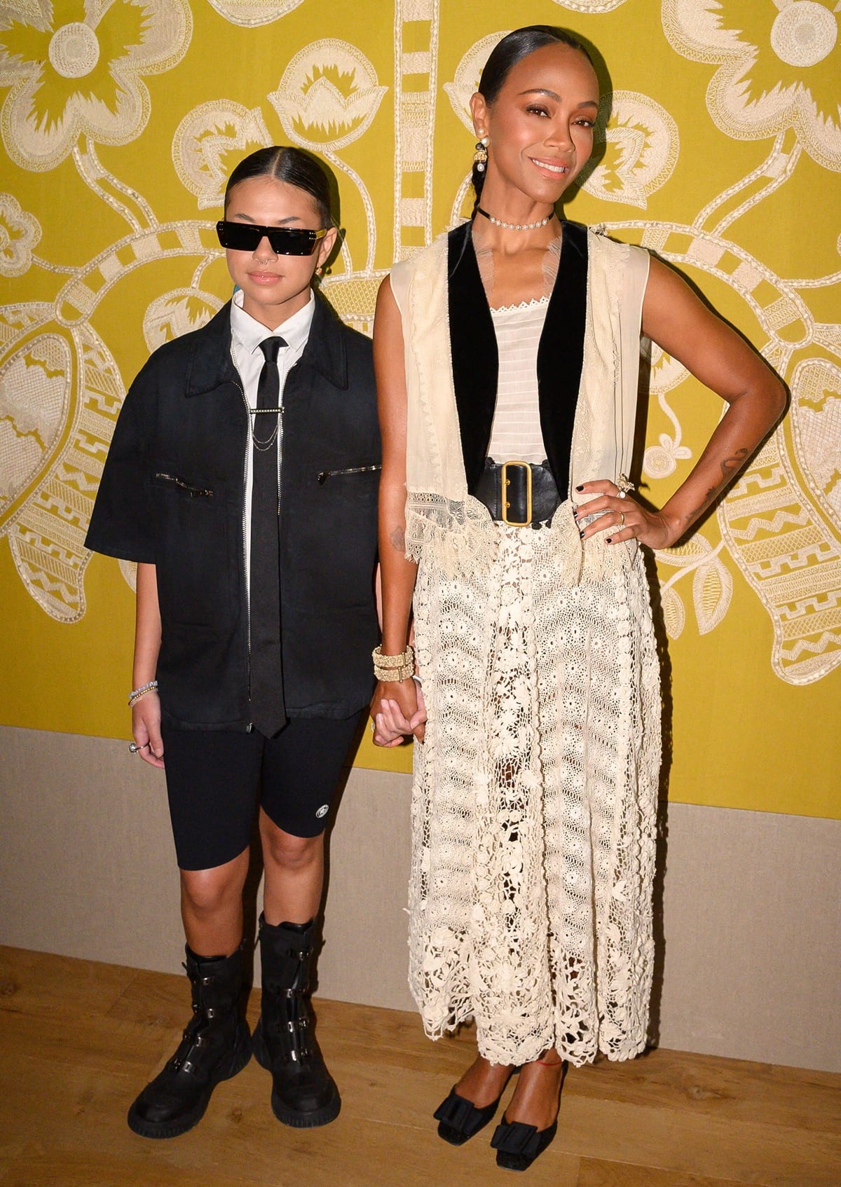 Zoe Saldana pairs a lace skirt with a velvet-trimmed vest and black bow heels, while holding hands with her niece, who sports a menswear-inspired look at the Dior Haute Couture Fall/Winter 2022-2023 show